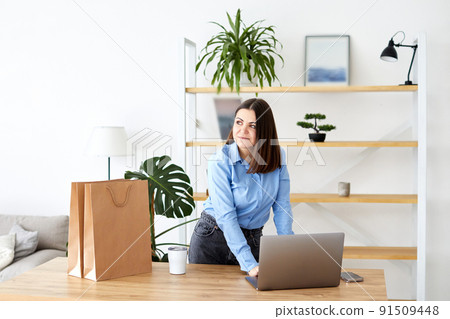 Happy businesswoman working in a home office standing looking at her laptop computer surrounded by gift bags and packaging for the products for sale on her new website Happy businesswoman working in a home office standing looking at her laptop computer surrounded by gift bags and packaging for the products for sale on her new website 91509448