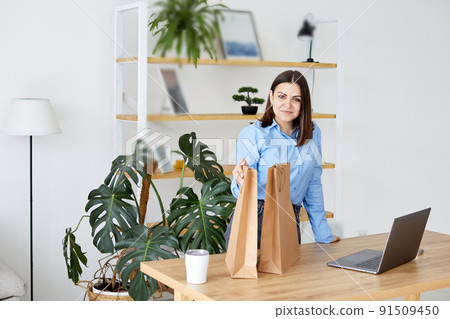 A woman looks in paper bags and considers her purchases, comparing with her laptop A woman looks in paper bags and considers her purchases, comparing with her laptop 91509450
