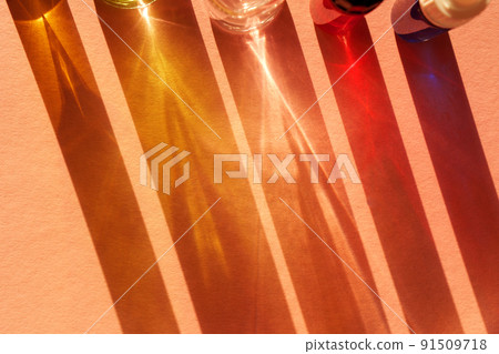 Different cosmetic glass bottles standing on pink background. Abstract pattern by shadows and reflections in the sunlight. Red, green and yellow shades. Flat lay style with copy space 91509718