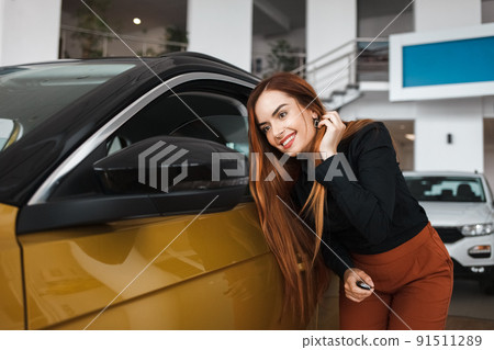 Young woman looks in the rearview mirror of a car at auto dealership. 91511289