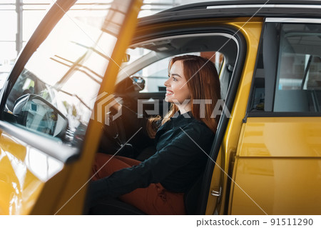 Girl inspects a new car for purchase. Young woman inside a car at dealership Girl inspects a new car for purchase. Young woman inside a car at dealership 91511290