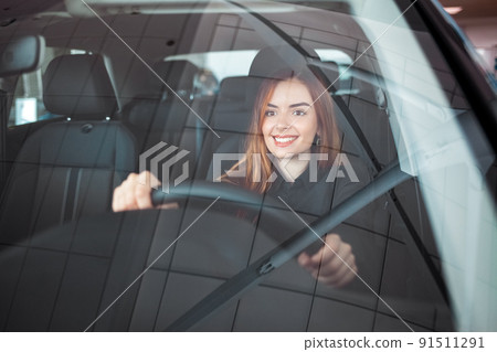 Smiling woman sitting at a car in a showroom. Smiling woman sitting at a car in a showroom. 91511291