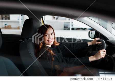 Smiling woman sitting at a car in a showroom. Smiling woman sitting at a car in a showroom. 91511293