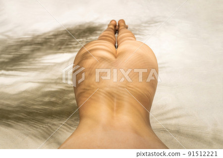 Naked beautiful buttocks of woman in a shadow under palm tree branches. Female relaxation on the sand beach at summer vacation. Top view 91512221