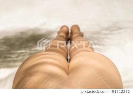 Naked beautiful buttocks of woman in a shadow under palm tree branches. Female relaxation on the sand beach at summer vacation. Top view 91512222