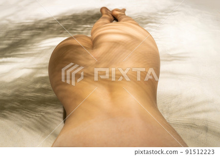 Naked beautiful buttocks of woman in a shadow under palm tree branches. Female relaxation on the sand beach at summer vacation. Top view 91512223