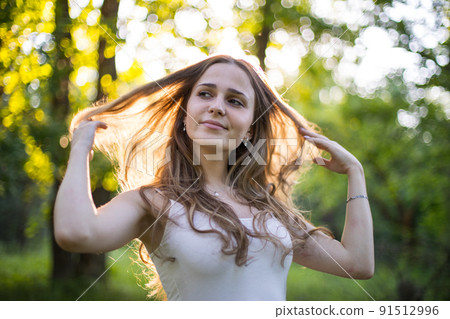 Beautiful young Russian girl dressed in a white dress, walks through the forest among the oaks in the rays of the sunset Beautiful young Russian girl dressed in a white dress, walks through the forest among the oaks in the rays of the sunset 91512996