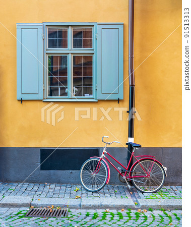 Red bicycle parked under old vintage traditional window with blue shutters in an orange wall at a cobblestone street 91513313
