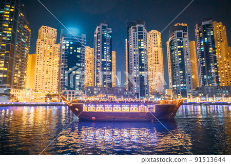 Tourist Boat, Sightseeing Boat Sailing On Dubai Marina At Nighttime. Night View Of high-rise buildings of residential Dubai Marina Is District in Dubai, United Arab Emirates. Holidays In United Arab Tourist Boat, Sightseeing Boat Sailing On Dubai Marina At Nighttime. Night View Of high-rise buildings of residential Dubai Marina Is District in Dubai, United Arab Emirates. Holidays In United Arab 91513644