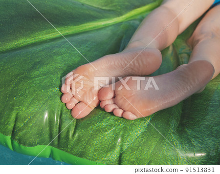 Feet on the inflatable floating bed on a hot summer day. Carefree lifestyle. Concept of relaxing, doing nothing, getting a tan Feet on the inflatable floating bed on a hot summer day. Carefree lifestyle. Concept of relaxing, doing nothing, getting a tan 91513831