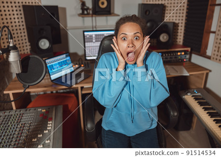 Surprised African American woman holds hands near her face and looks at camera with astonishment in sound engineer room 91514534