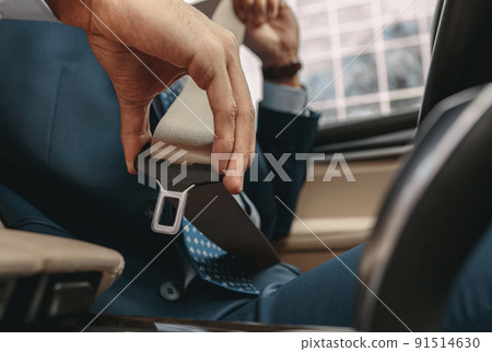 Image of man sitting behind steering wheel of his car and fastening seat belt 91514630