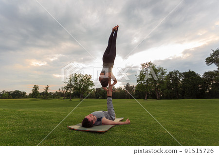 Man lying on grass and balancing woman in his feet. Young couple doing acro yoga in park 91515726