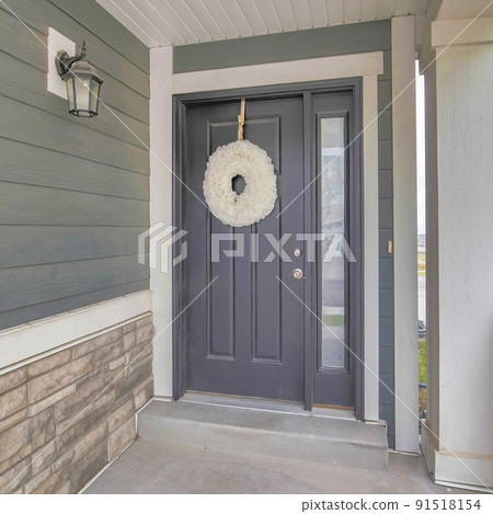 Square frame Gray front door with white holiday wreath and narrow sidelight at home facade 91518154