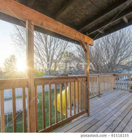 Square frame Wooden deck of house with yellow slide going down to the yard with trampoline 91518155
