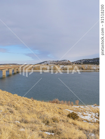 Vertical A clear and peaceful lake with snow on the edge and bridge to the side Vertical A clear and peaceful lake with snow on the edge and bridge to the side 91518200