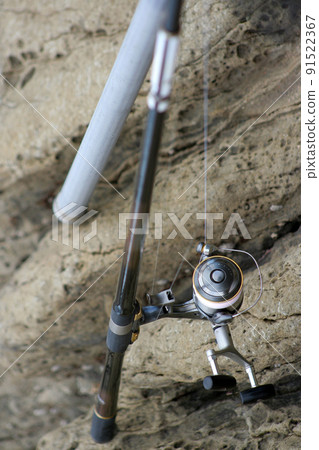 A photo of a reel of double counterclaim with a brake leaning against a rock on the beach, a fine rod, and a pattern of a ball net. A photo of a reel of double counterclaim with a brake leaning against a rock on the beach, a fine rod, and a pattern of a ball net. 91522367