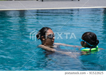 Cute little girl having fun swimming with her mother in the pool on a sunny day. Happy family, mother and her daughter playing in the swimming pool. Summer lifestyle concept. 91522625