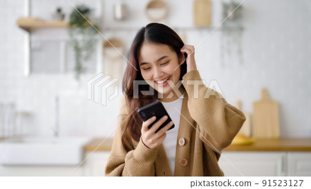 Asia female standing at counter kitchen and using mobile smartphone Asia female standing at counter kitchen and using mobile smartphone 91523127