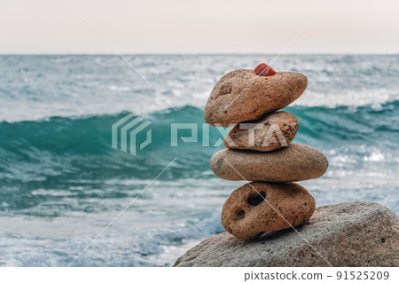 Balanced pebble pyramid on the beach on a sunny day. Sea foam on the background. Selective focus. Zen stones on the sea beach, meditation, spa, harmony, calmness, balance concept 91525209