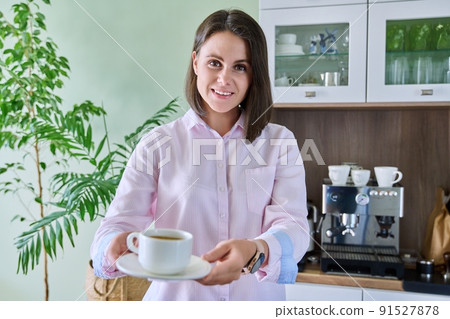 Young woman offering cup of coffee, home kitchen interior coffee machine background Young woman offering cup of coffee, home kitchen interior coffee machine background 91527878