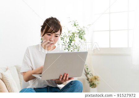 Japanese woman having trouble looking at a computer on the sofa 91527972
