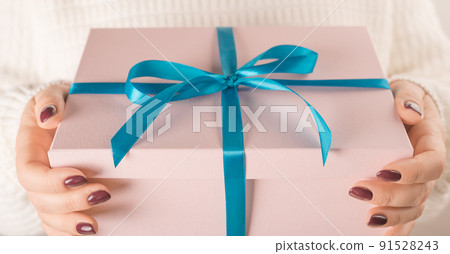 Hands holding pink gift box in package with blue ribbon. Female hands holding Valentine day gift box on white 91528243