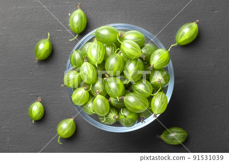 Ripe green gooseberries in a glass transparent bowl and jar on a black  background.  91531039