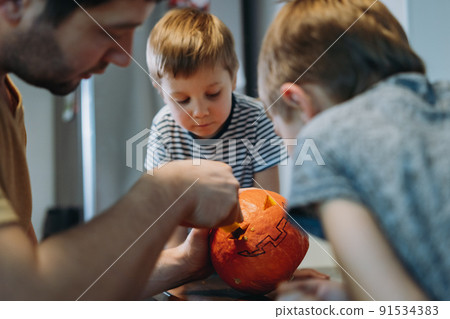 Caucasian man with his cute sons carving out eyes on a pumpkin to make traditional Jack lantern. 91534383