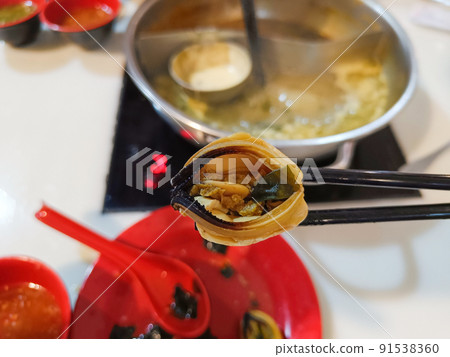 Man uses chopsticks to pick up mussels while eating a hot pot. Man uses chopsticks to pick up mussels while eating a hot pot. 91538360