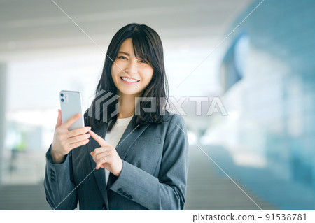 A business woman in a young suit looking at a smartphone at the entrance of the office 91538781
