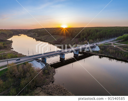 Beautiful view of the bridge across the Iset river in the city of Kamensk-Uralsky at sunset in spring. Kamensk-Uralskiy, Sverdlovsk region, Ural mountains, Russia. 91540585