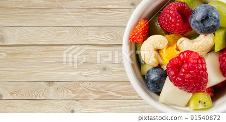 Bowl of healthy fresh fruit salad on wooden table. top view copy space. modern fruit salad light wooden background, 91540872