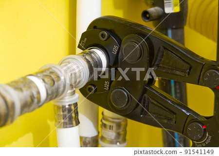 Worker connecting alupex pipes with a tap. Hand press for water pipes PEX - AL - PE-X. plumbing industry. Worker connecting alupex pipes with a tap. Hand press for water pipes PEX - AL - PE-X. plumbing industry. 91541149