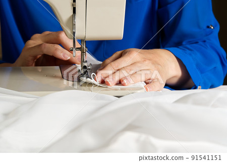 A woman works on a sewing machine. seamstress sews white curtains, close up view. 91541151