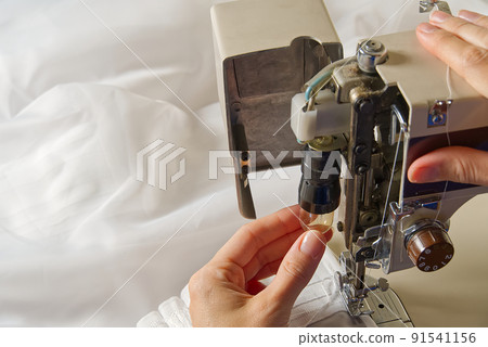 Woman's hands setting sewing machine. worker changing bulb in sewing machine. 91541156