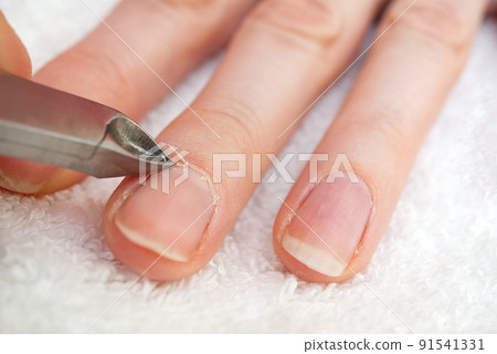 Woman's hand removing nail cuticle on light white table. Care about dry, overgrown cuticle. Closeup. 91541331