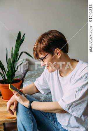 Woman with short hair at home sitting on the floor with her smartphone Woman with short hair at home sitting on the floor with her smartphone 91541818
