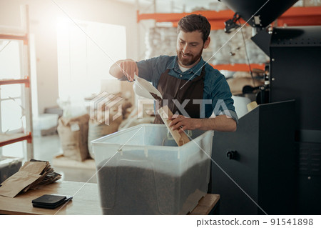 Uniformed worker packs roasted coffee beans into packages for sale 91541898