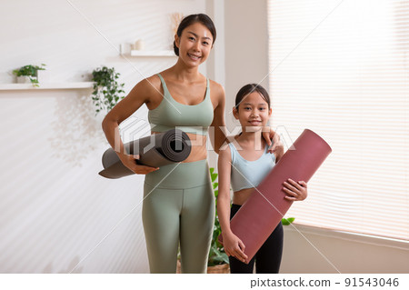 Happy Asian mom and little girl holding yoga mat smile and laughing together ready to exercise yoga at home.2 Healthy mother and daughter cheerful with yoga workout in warmth place.good moment 91543046