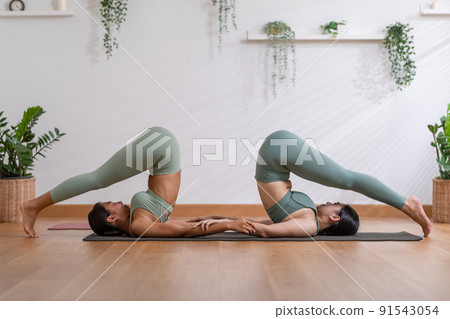 Couple and paired Asian young woman on yoga mat doing breathing exercise yoga Halasana or Plough pose together.Yoga meditation of two healthy female balancing body and relax cozy home. Wellness life Couple and paired Asian young woman on yoga mat doing breathing exercise yoga Halasana or Plough pose together.Yoga meditation of two healthy female balancing body and relax cozy home. Wellness life 91543054