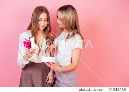 beautiful and attractive woman gives a box with gift to her teenager daughter on a pink background in the studio . the concept of celebrating the mother's day and birthday 91543689