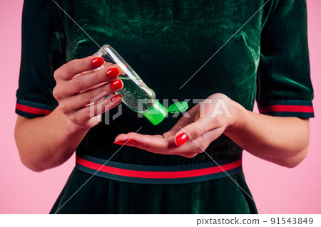 Woman hand applying hand sanitizer on a pink background in the studio 91543849
