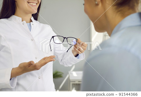 Friendly female optician works with patient and shows her new glasses for testing and trying. Friendly female optician works with patient and shows her new glasses for testing and trying. 91544366
