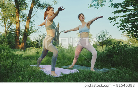 Two young women doing yoga virabhadrasana outdoor Two young women doing yoga virabhadrasana outdoor 91546398