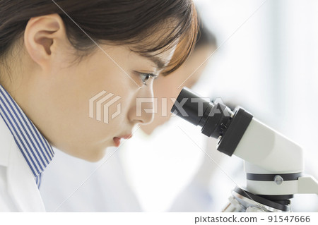 A woman in a white coat looking through a microscope A woman in a white coat looking through a microscope 91547666