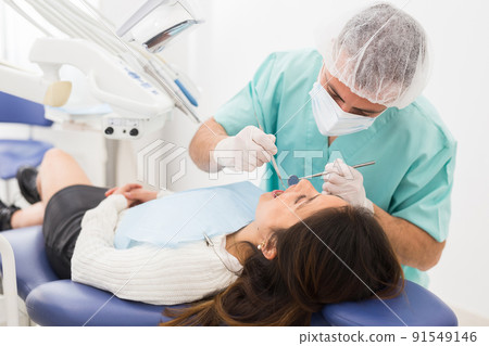 Dentist man examining a latin female patient teeth 91549146