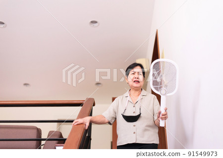 Elderly asian woman using mosquito swatter at home,Elderly women with mosquito electric net racket 91549973