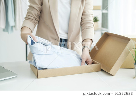 Asian female clothes shop owner folding a t-shirt and packing in a cardboard parcel box. Asian female clothes shop owner folding a t-shirt and packing in a cardboard parcel box. 91552688