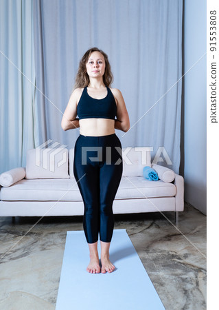 Young healthy beautiful woman in sports top and leggings practicing yoga at home, standing in pose on yoga mat Young healthy beautiful woman in sports top and leggings practicing yoga at home, standing in pose on yoga mat 91553808